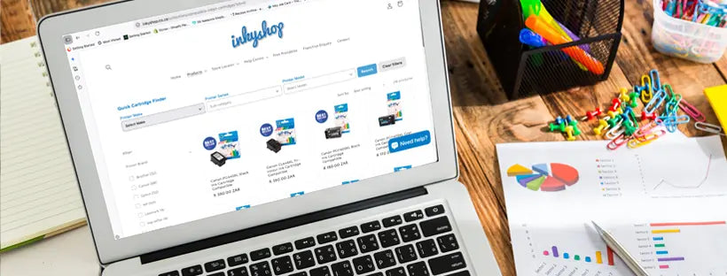 A modern laptop displaying The Inky Shop website on a desk surrounded by vibrant color-printed pie charts and high-quality office stationery, showcasing professional print solutions.